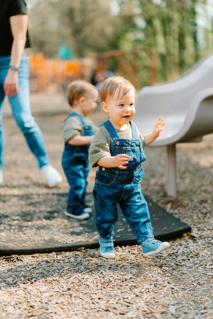 Two toddlers in denim overalls at a playground